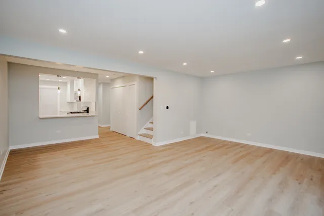 a view of empty room with wooden floor and kitchen view