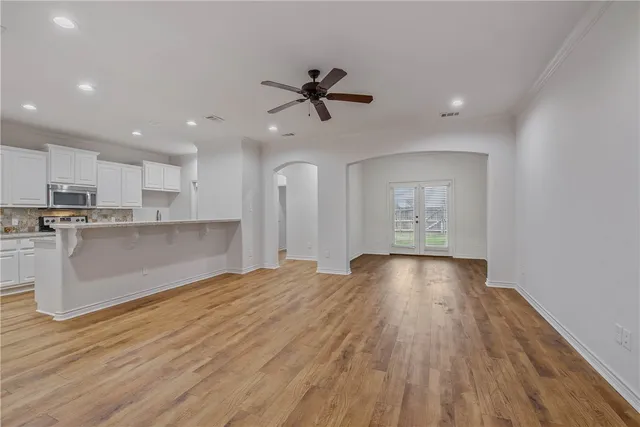 a view of an empty room and kitchen with wooden floor and window