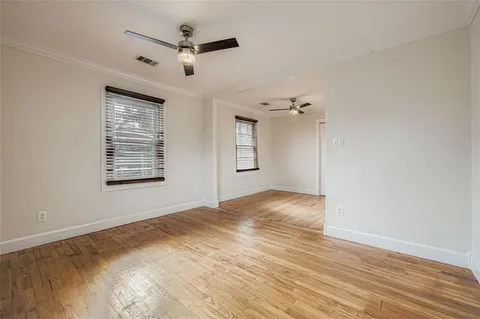 a view of an empty room with wooden floor and a ceiling fan