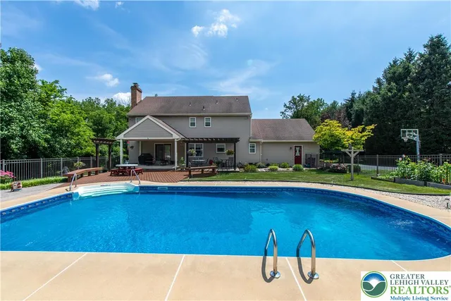 a view of pool with lawn chairs and large trees