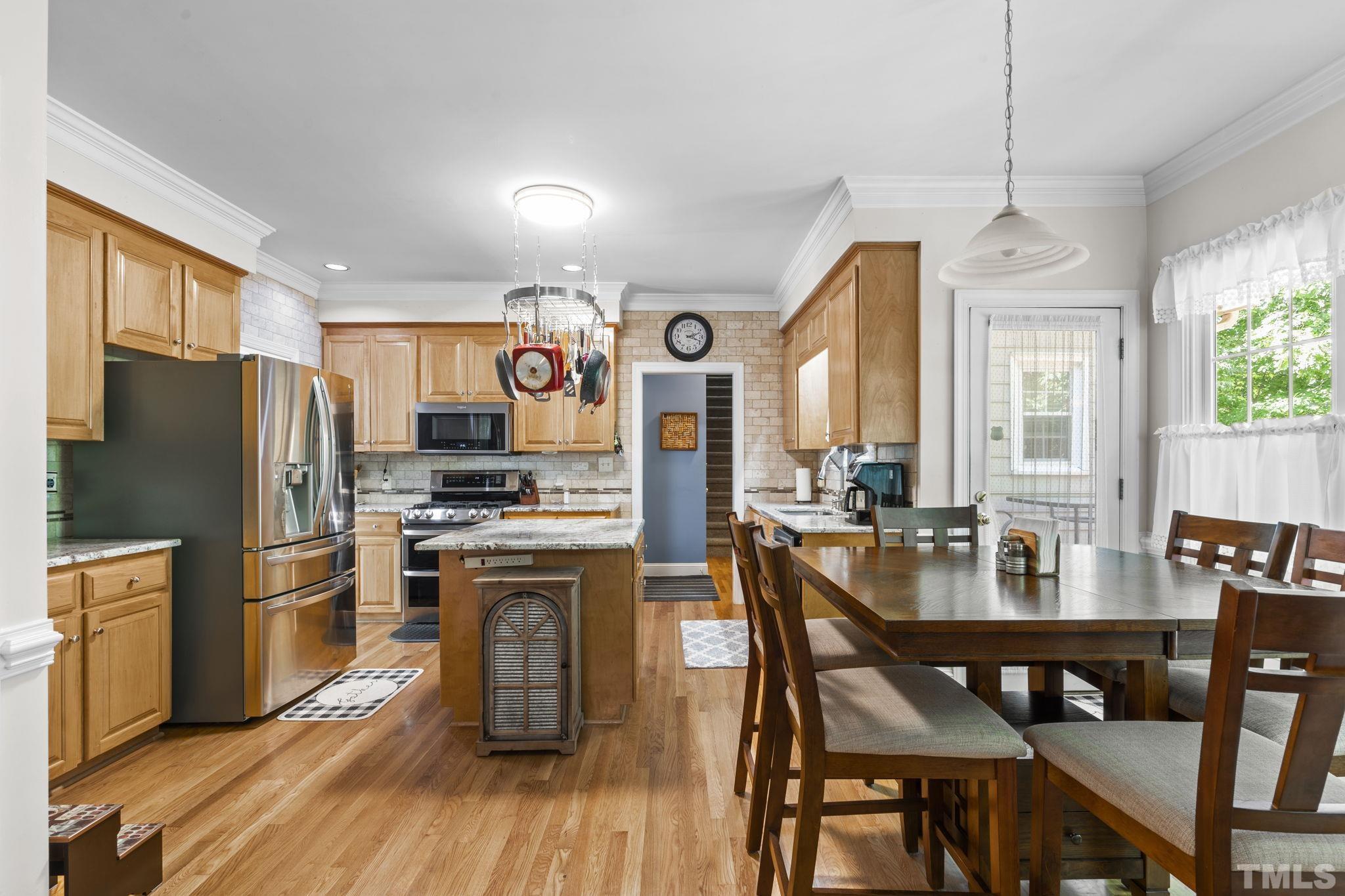 7705 Tylerton Drive Raleigh, NC 27613 - Photo 8 of 35 a kitchen with stainless steel appliances granite countertop a stove a refrigerator a dining table and chairs with wooden floor