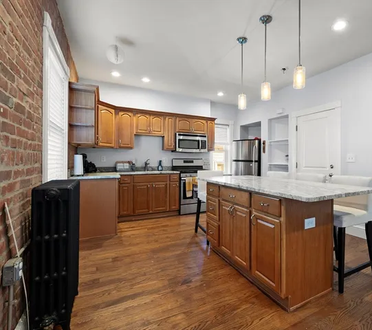 a kitchen with stainless steel appliances granite countertop wooden cabinets a refrigerator a sink a stove and a wooden floors