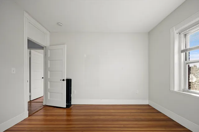 a view of an empty room with window and wooden floor