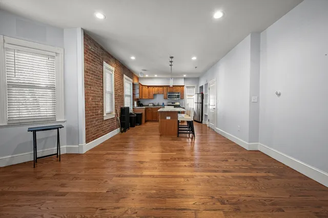 a view of an empty room with kitchen and windows