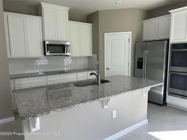 a kitchen with stainless steel appliances granite countertop a sink a microwave a refrigerator and white cabinets