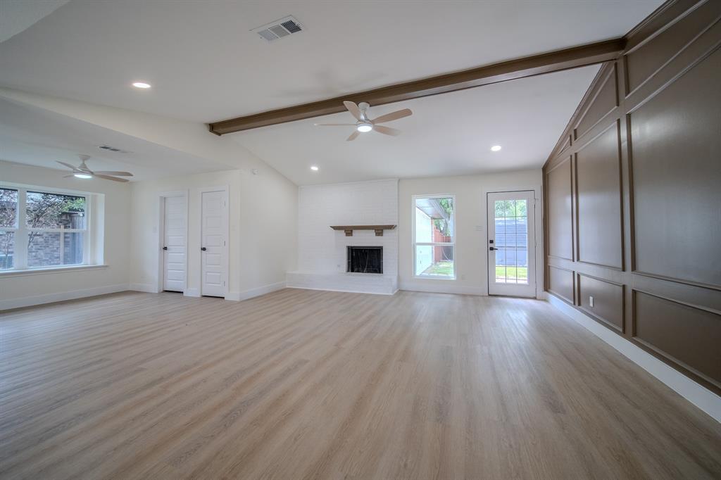 142 Ridgegate Drive Garland, TX 75040 - Photo 9 of 26 Spacious interior featuring wood-finish flooring, a white brick fireplace with a wood mantel, and a decorative paneled accent wall