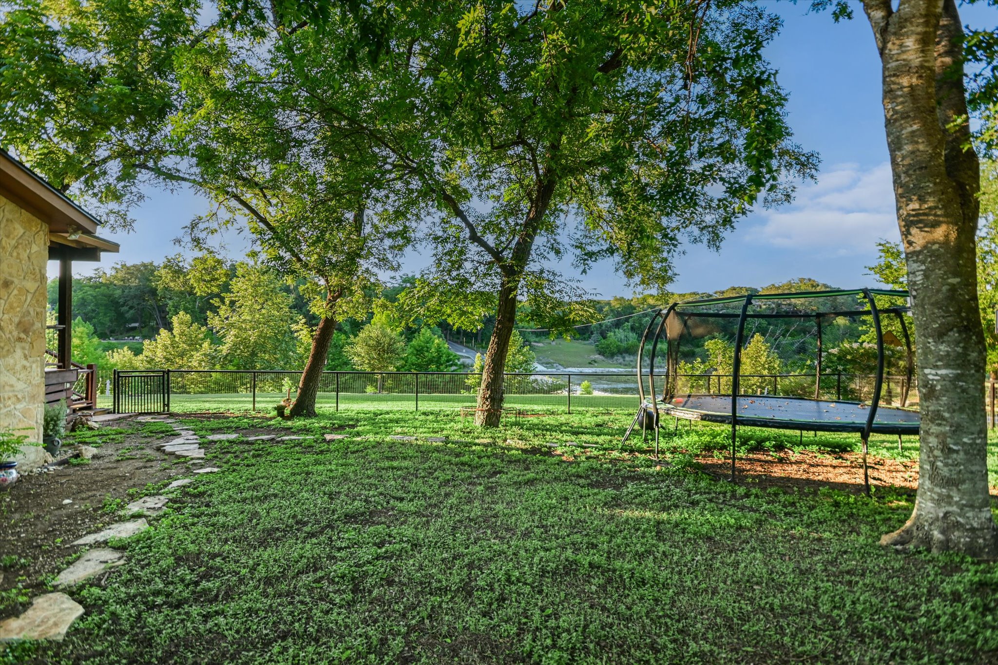 2411 Spoke Hollow Road Wimberley, TX 78676 - Photo 23 of 37 A peaceful backyard retreat features a grassy lawn, stone path, and a black fence offering serene water views.