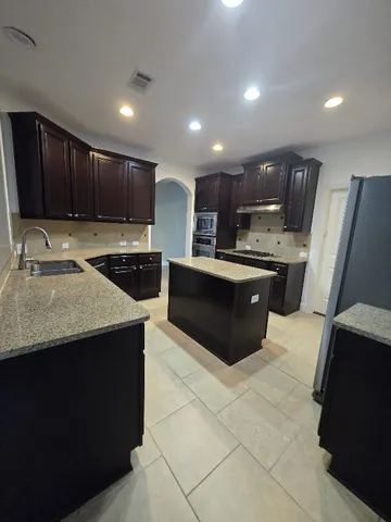 a kitchen with kitchen island granite countertop a sink counter top space cabinets and stainless steel appliances