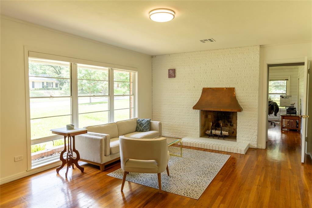 3228 Colcord Avenue Waco, TX 76707 - Photo 23 of 29 Living area featuring hardwood flooring, a white-painted brick fireplace with a copper hood, and a large window overlooking exterior landscaping