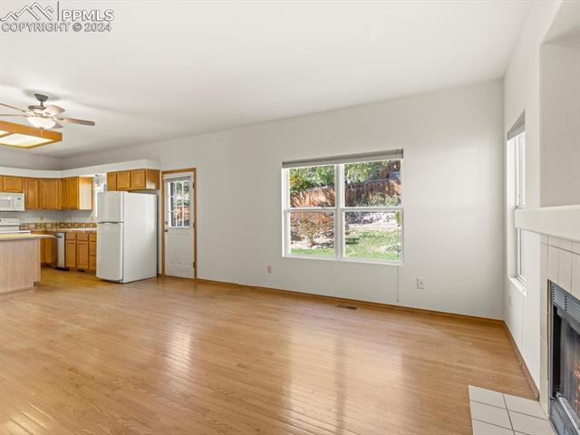 7590 Julynn Road Colorado Springs, CO 80919 - Photo 22 of 44 Unfurnished living room featuring a tiled fireplace, light hardwood / wood-style floors, and ceiling fan