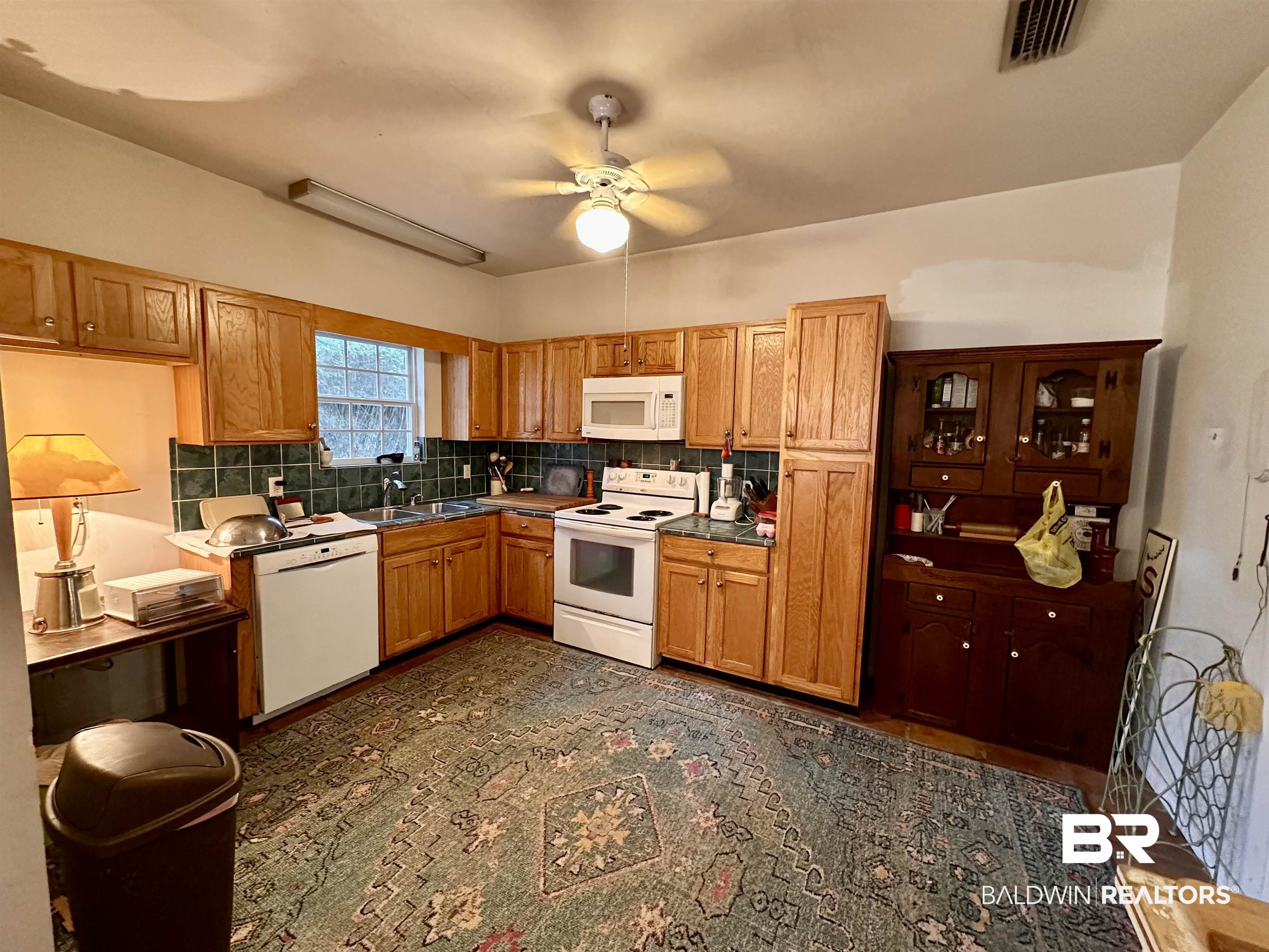 9101 Coronada Road Elberta, AL 36530 - Photo 6 of 27 Kitchen featuring white appliances, backsplash, ceiling fan, brown cabinetry, and dark countertops