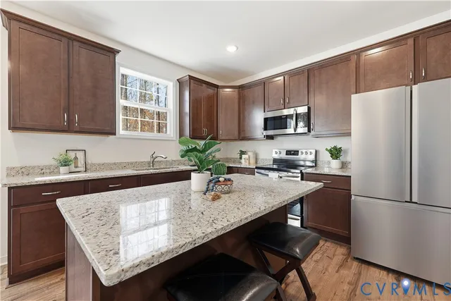 a kitchen with granite countertop a refrigerator a stove a sink dishwasher and wooden cabinets with wooden floor