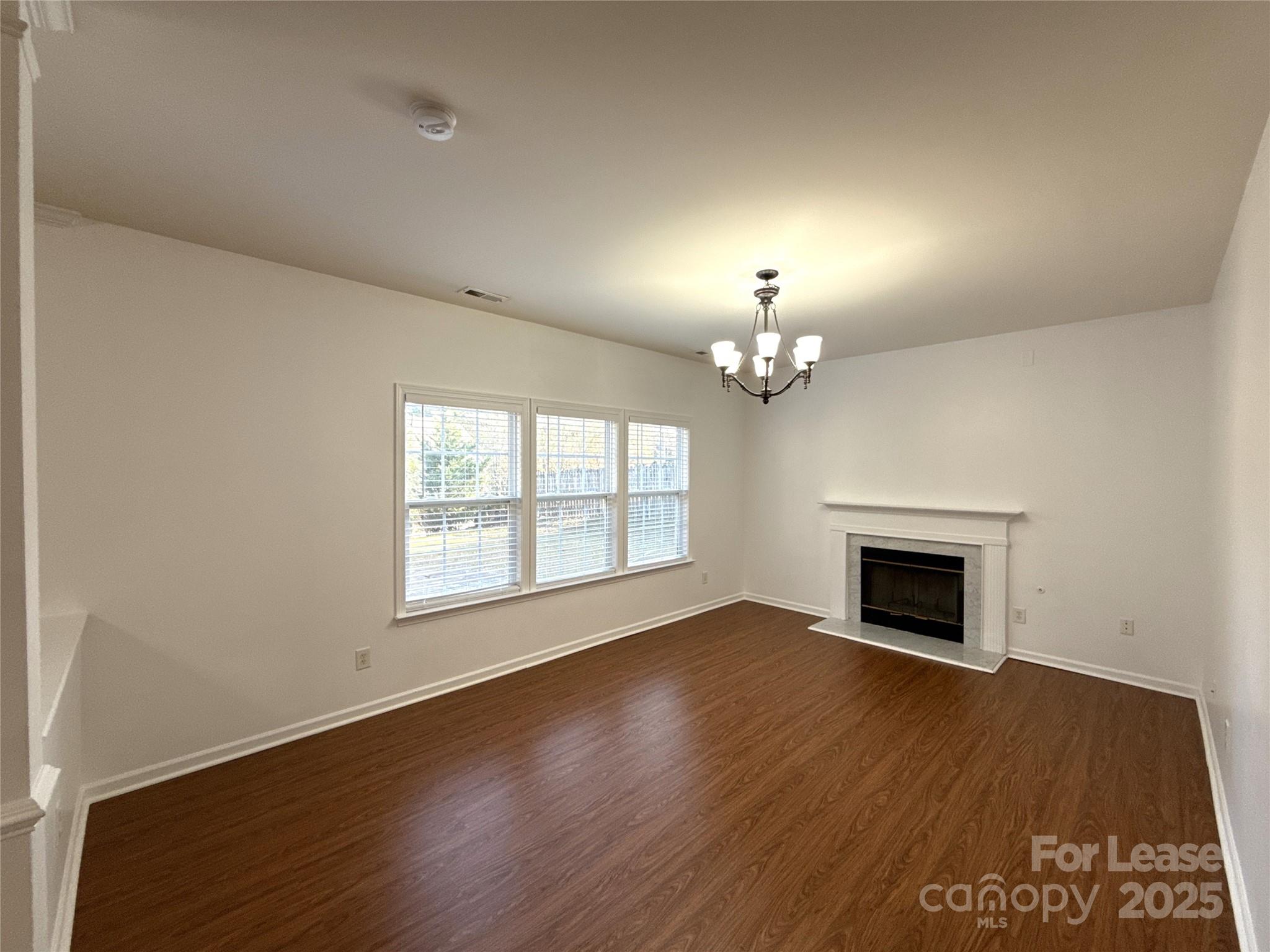 3415 Cole Mill Road Charlotte, NC 28270 - Photo 6 of 18 an empty room with wooden floor chandelier and fireplace