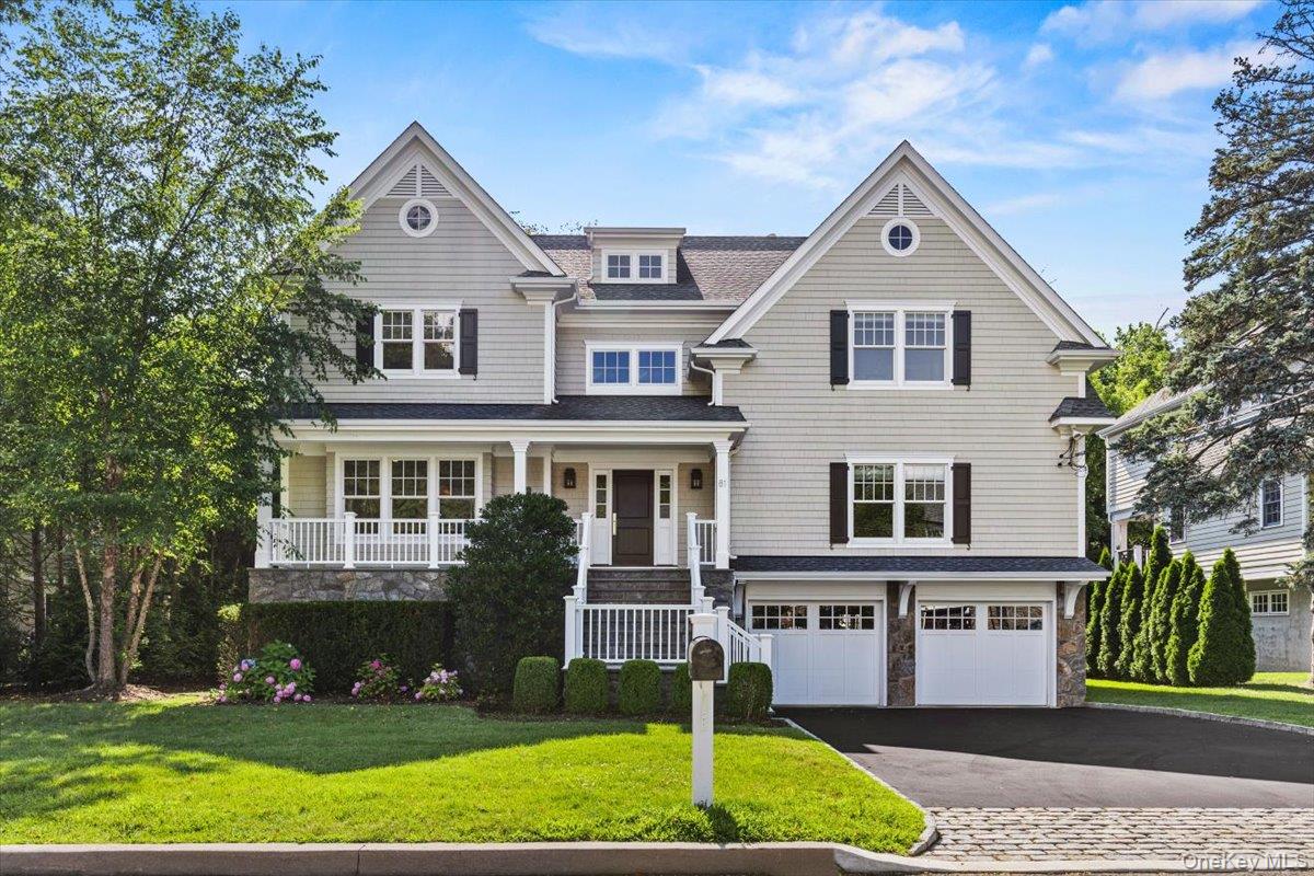 Shingle-style home with stone siding, a garage, driveway, a front lawn, and covered porch