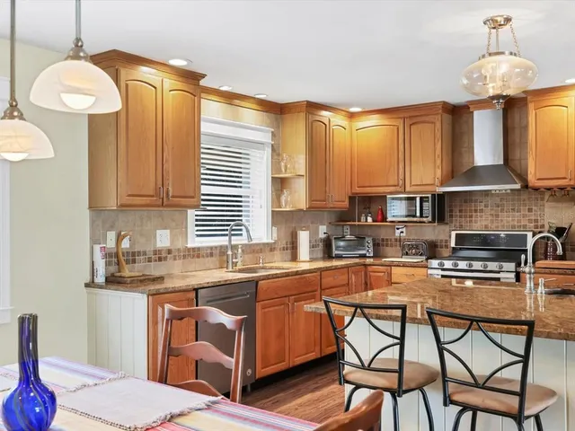 a kitchen with stainless steel appliances granite countertop a refrigerator a sink a stove and white cabinets with wooden floor