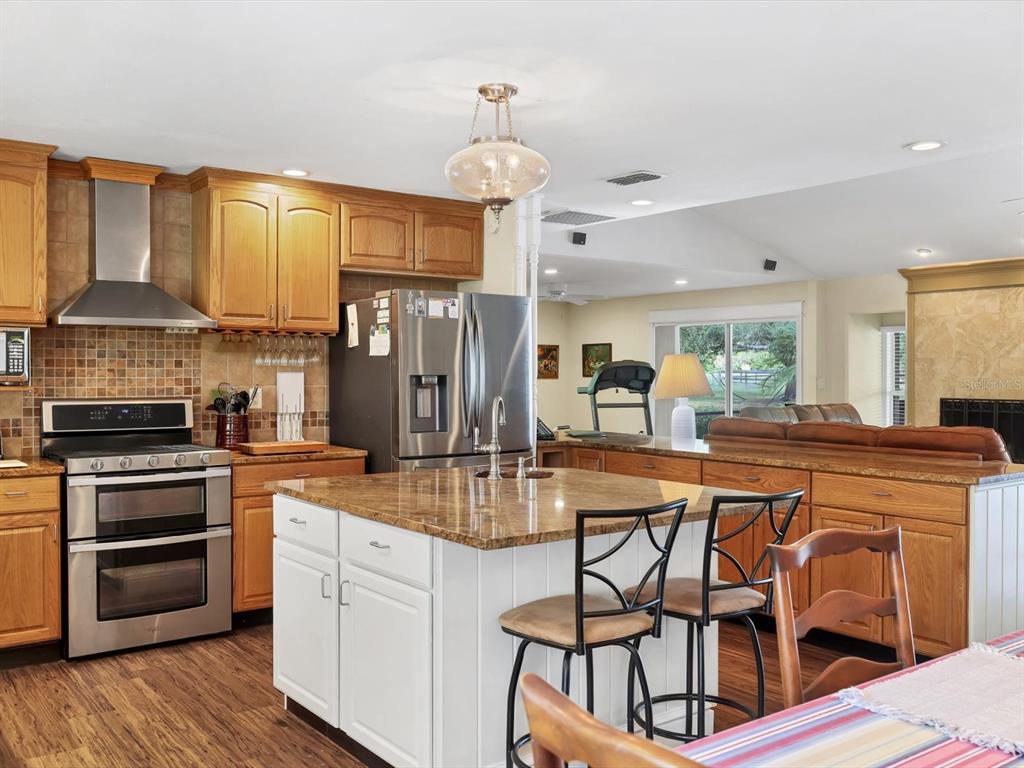 4708 Hidden River Road Sarasota, FL 34240 - Photo 19 of 67 a kitchen with stainless steel appliances kitchen island granite countertop a stove a refrigerator a oven a dining table and chairs with wooden floor