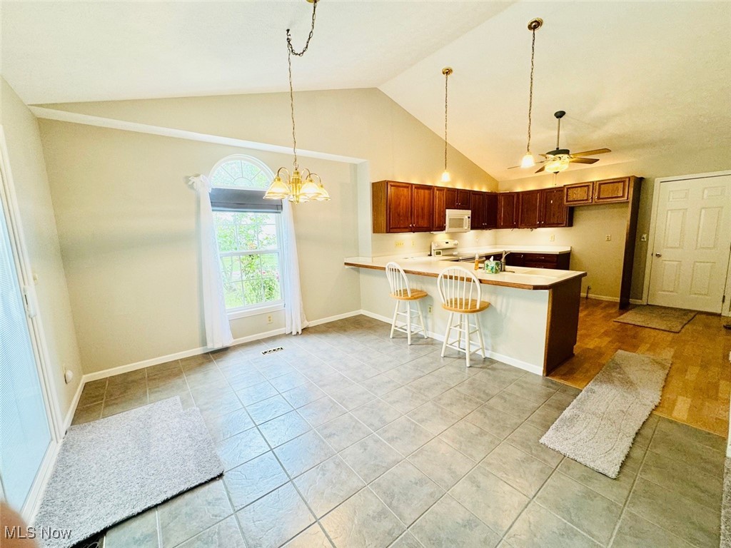 1467 Bennett Road Madison, OH 44057 - Photo 16 of 26 Kitchen featuring ceiling fan with notable chandelier, lofted ceiling, kitchen peninsula, a kitchen bar, and white appliances