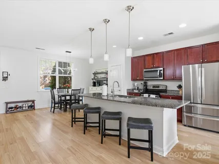 a kitchen with stainless steel appliances granite countertop a stove a refrigerator a kitchen island a dining table and chairs with wooden floor