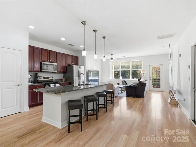 a open kitchen with stainless steel appliances granite countertop a stove top oven a refrigerator a dining table and chairs with wooden floor