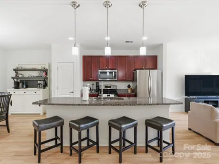 a kitchen with stainless steel appliances granite countertop a stove a sink a microwave a refrigerator and chairs