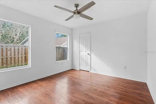 an empty room with wooden floor chandelier fan and windows