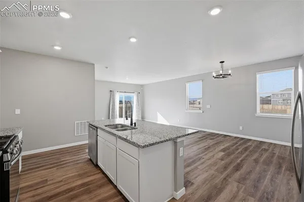 a large white kitchen with kitchen island a sink wooden floor and stainless steel appliances