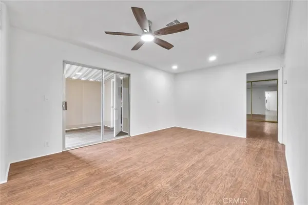 a view of an empty room with wooden floor and a ceiling fan