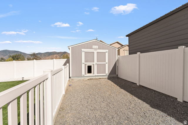 3678 Spiral Springs Road, Unit 204 Tooele, UT 84074 - Photo 48 of 59 Detached storage shed, gravel ground cover, white vinyl fencing, and mountain backdrop