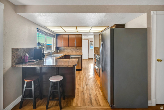10 North Main Street Centerfield, UT 84622 - Photo 12 of 52 Kitchen featuring appliances with stainless steel finishes, a breakfast bar, a peninsula, light wood finished floors, and brown cabinetry