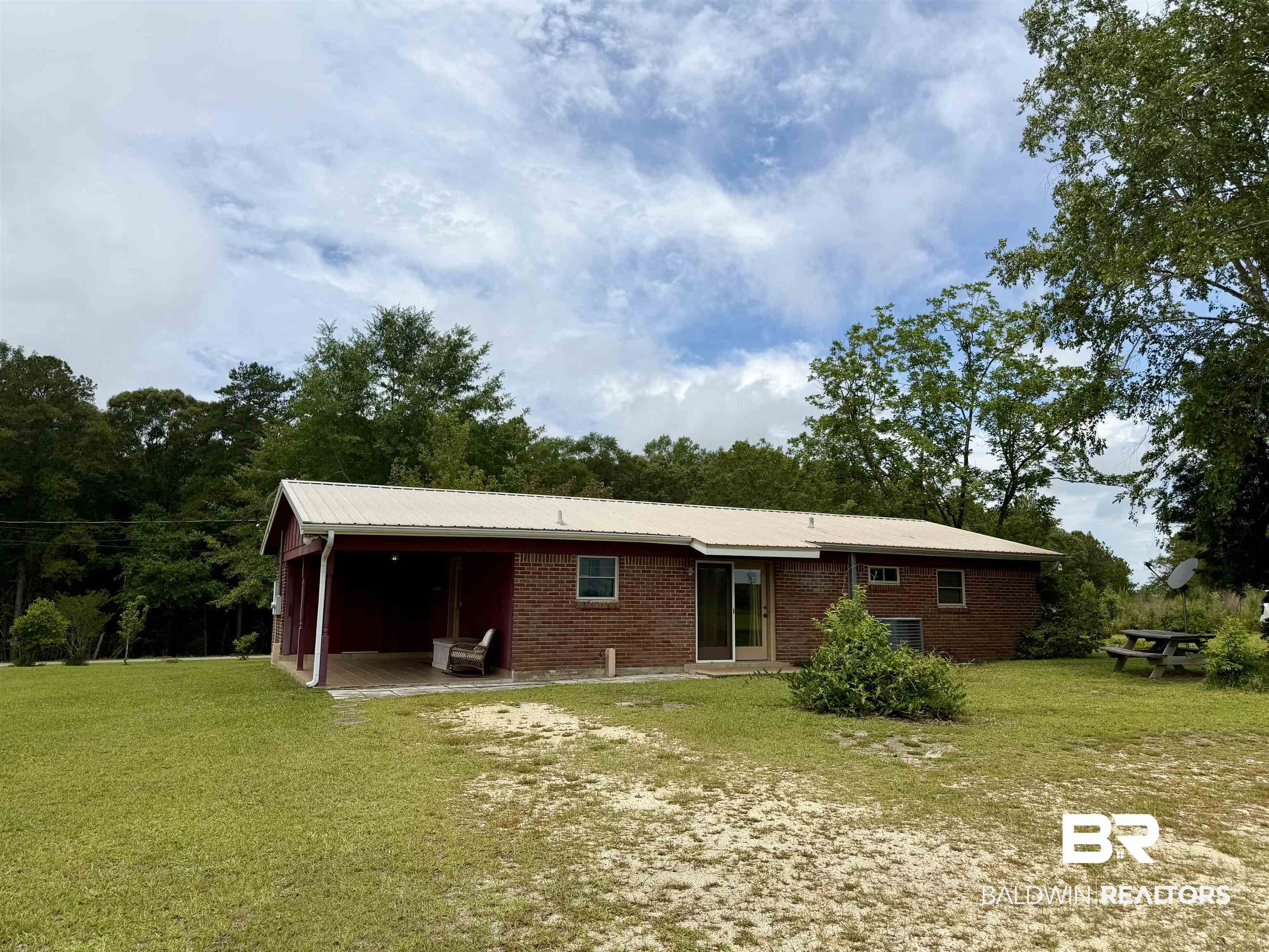 3642 Old Castleberry Road Brewton, AL 36426 - Photo 13 of 14 Brick exterior residence with a metal roof, featuring a covered carport, expansive front lawn, and surrounding mature trees