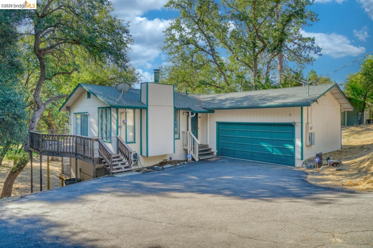 19215 Ferretti Road Groveland, CA 95321 - Photo 1 of 40 Split-level residence featuring a teal garage door, a front-facing deck with wood railings, and a prominent chimney