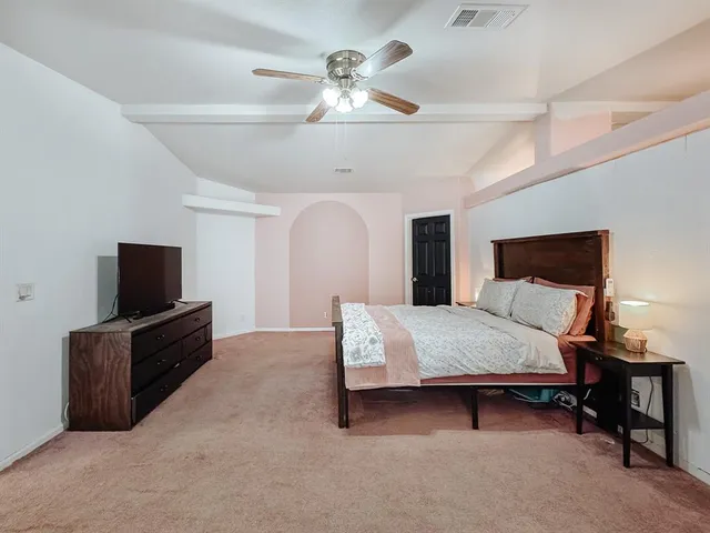 a spacious bedroom with a bed and a flat tv screen on dresser
