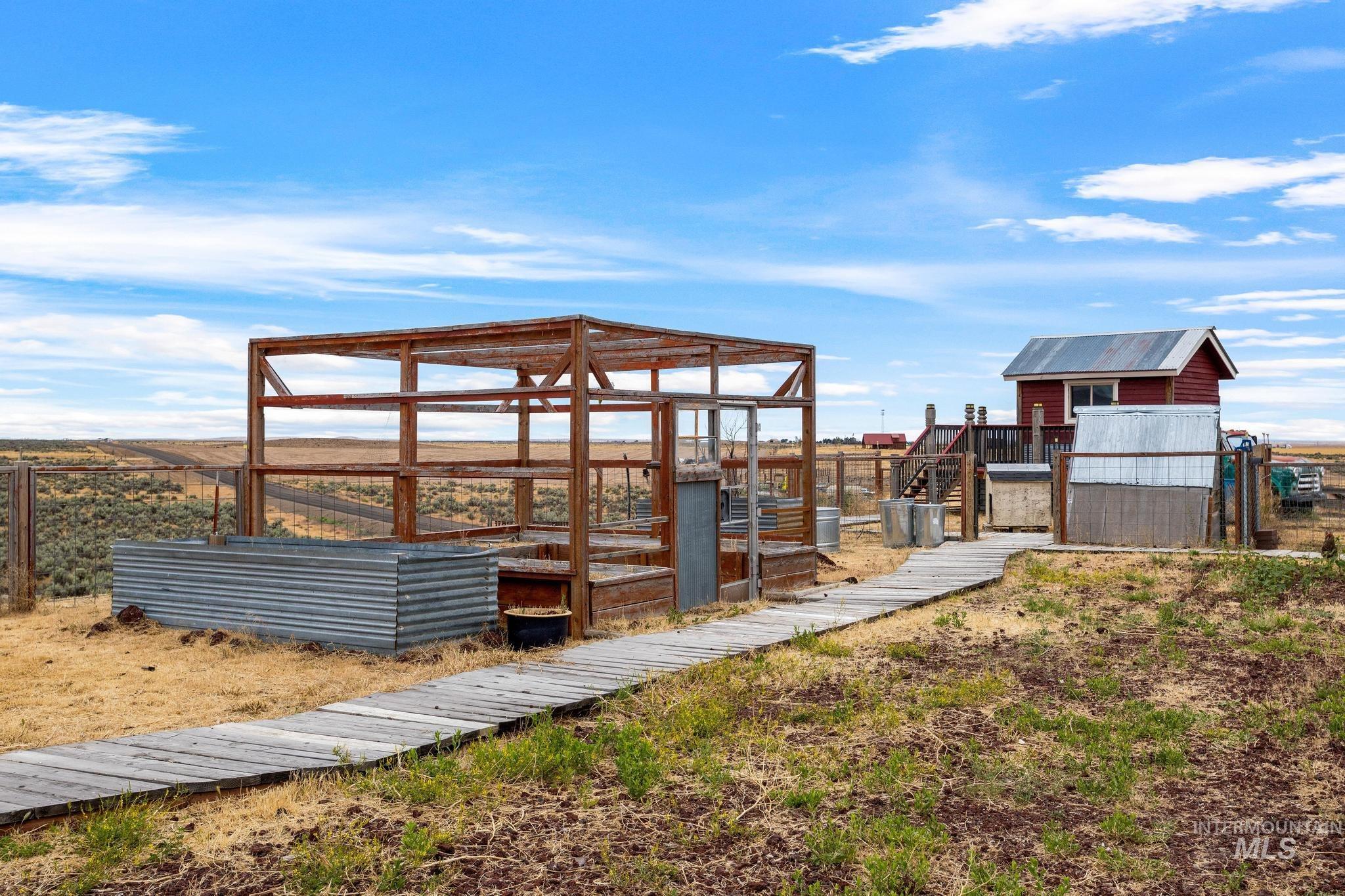 870 Desert Wind Road Boise, ID 83716 - Photo 50 of 50 Outdoor wood-framed structure with a corrugated metal planter box, a wooden pathway, and a red-sided outbuilding featuring a metal roof