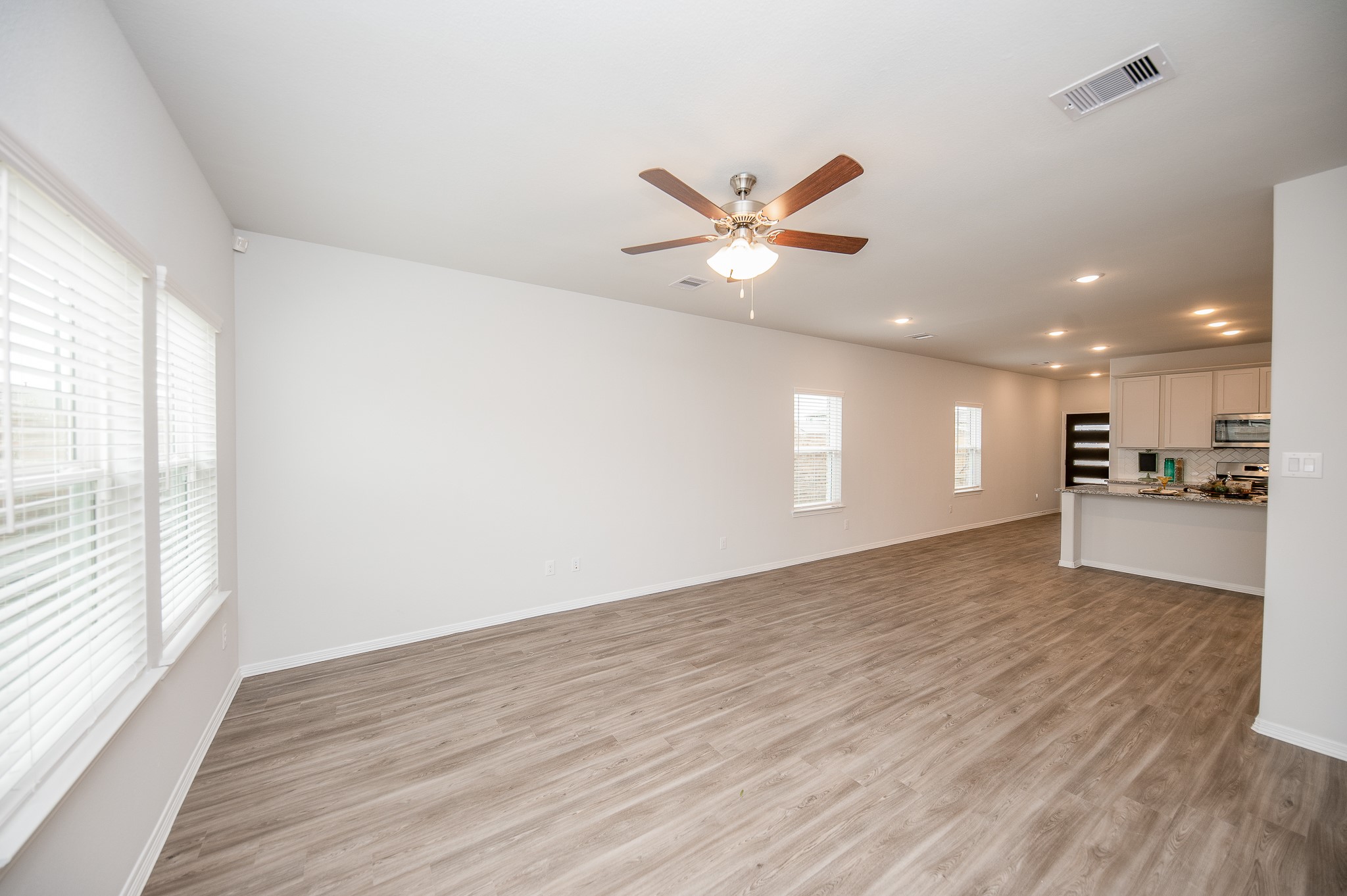 23302 Spring Genesis Lane Katy, TX 77493 - Photo 17 of 32 Spacious open-concept living area features sleek wood-style flooring, and ample natural light from large windows. It flows seamlessly into a modern kitchen with white cabinetry and stainless steel appliances, perfect for entertaining.