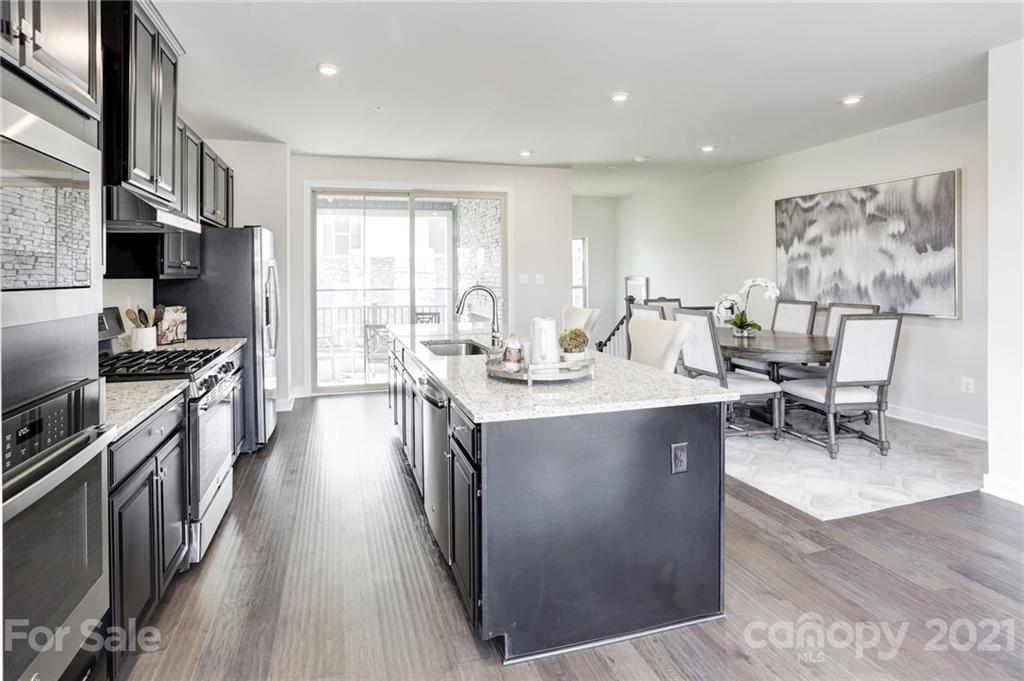 957 Portrush Lane, Unit 1010D Tega Cay, SC 29708 - Photo 5 of 13 a large kitchen with stainless steel appliances a stove a sink dishwasher and a dining table with wooden floor