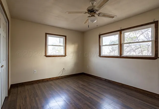 an empty room with wooden floor fan and windows