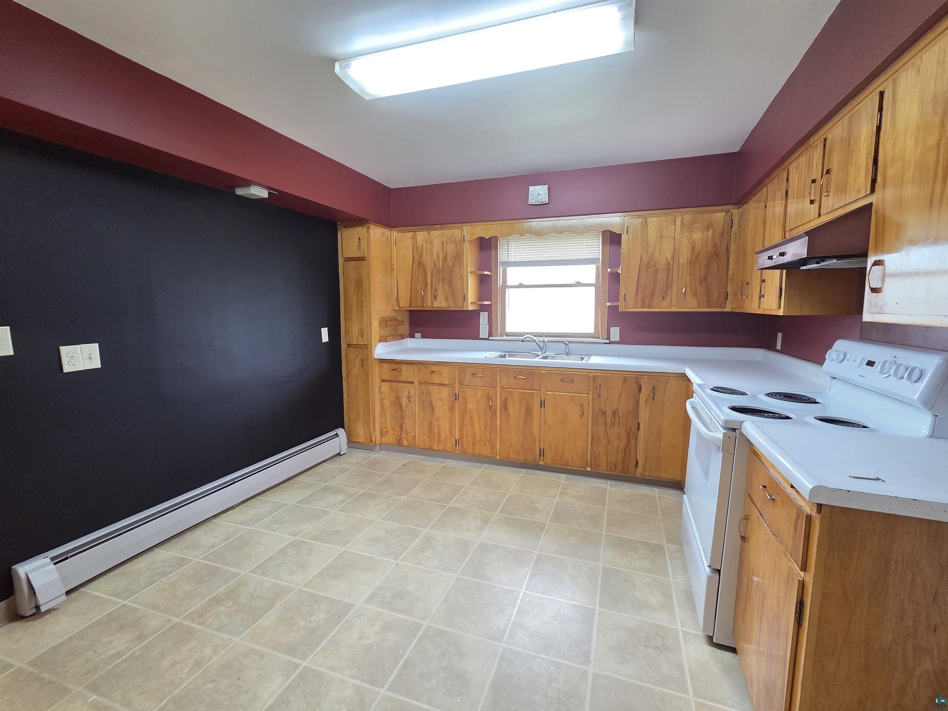 56 East 2nd Street Superior, WI 54880 - Photo 7 of 18 Kitchen featuring extensive wood cabinetry, white countertops, a double basin sink beneath a window, and a built-in range