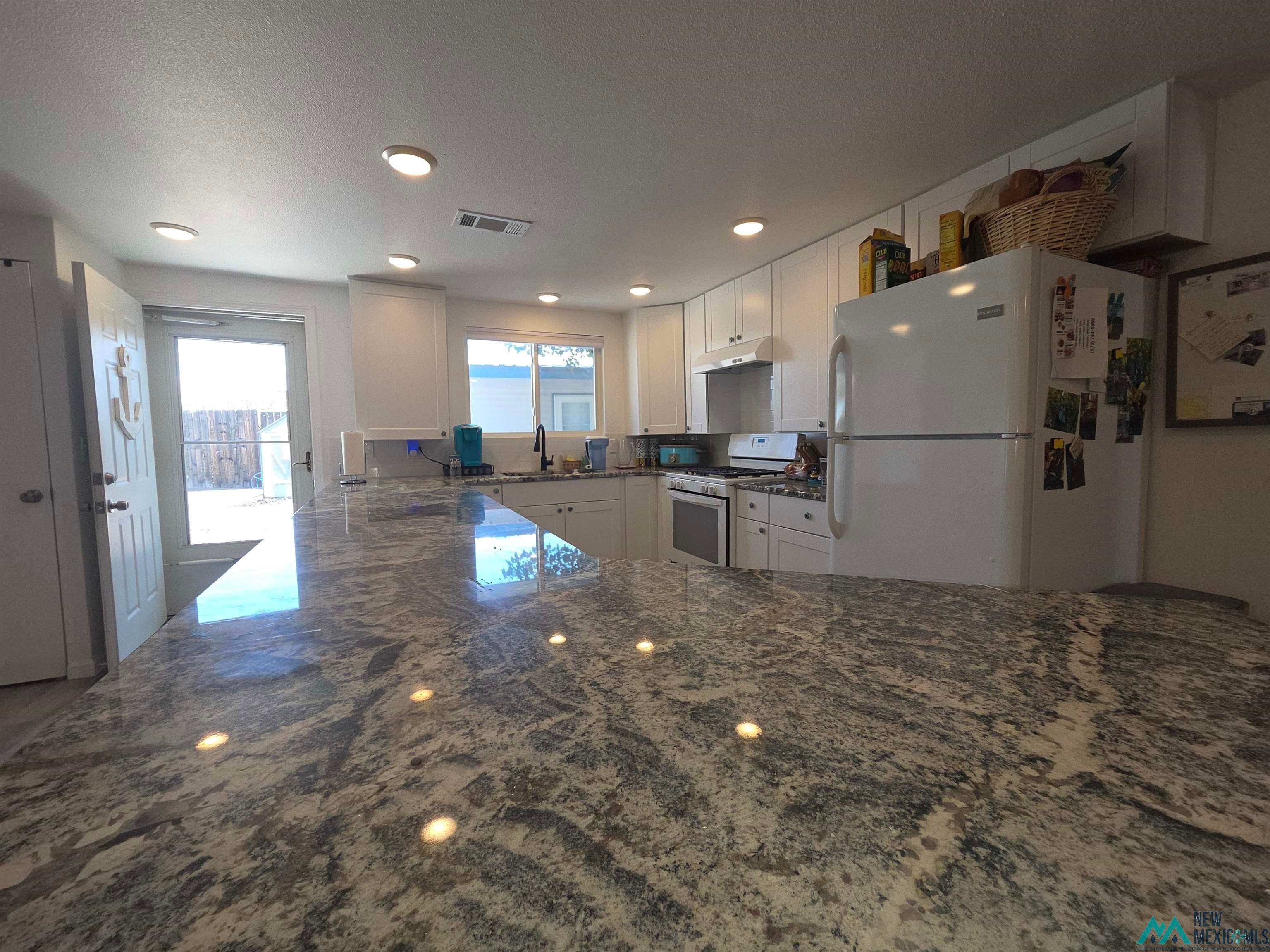 407 Bass Road Elephant Butte, NM 87935 - Photo 24 of 54 Kitchen with dark stone counters, white cabinets, white appliances, a textured ceiling, and recessed lighting