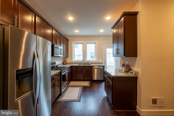 a kitchen with stainless steel appliances granite countertop a refrigerator a sink dishwasher a stove and white countertops with wooden floor