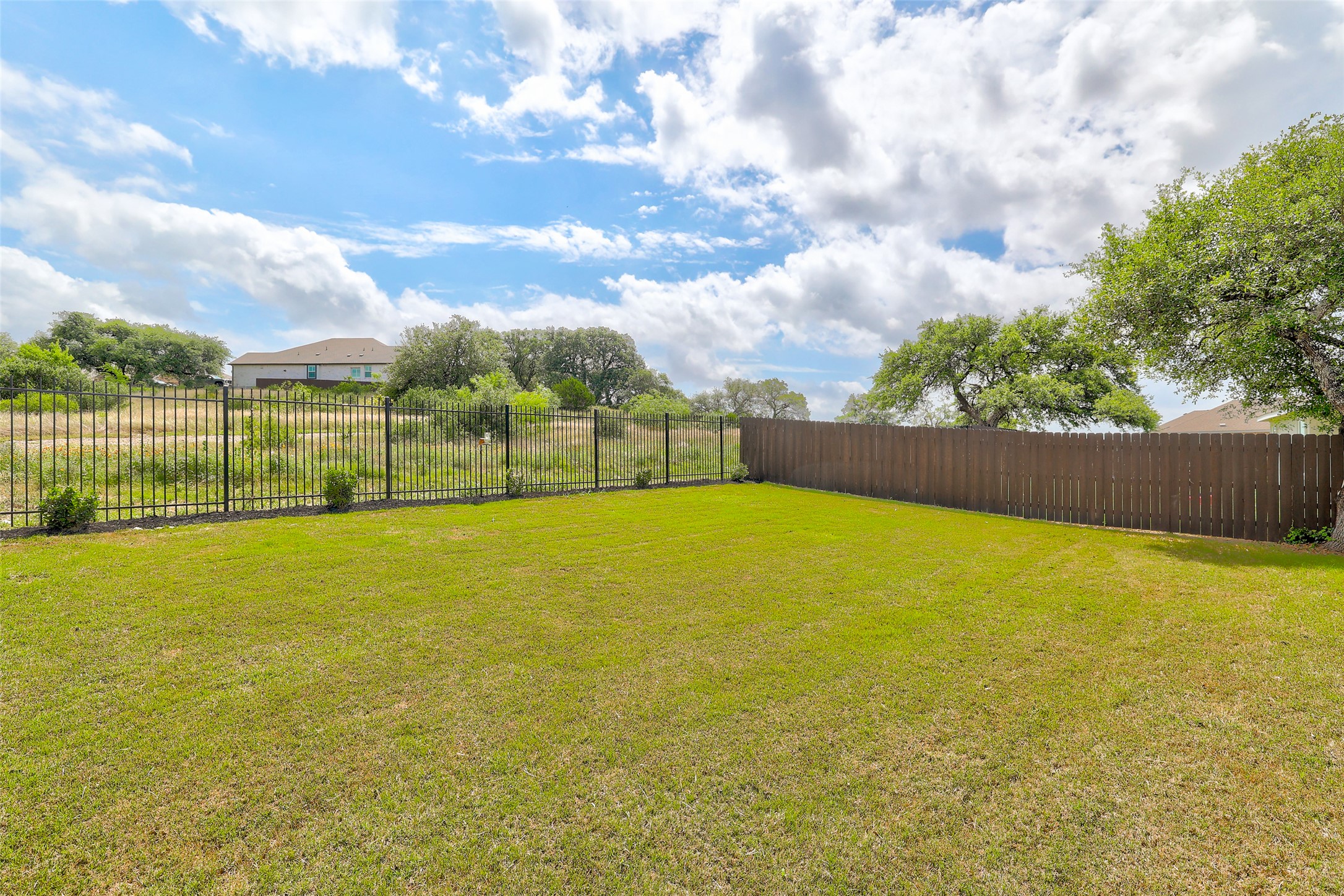 2333 Four Waters Loop Georgetown, TX 78628 - Photo 32 of 35 Expansive green lawn with a dark wood privacy fence and a black metal fence bordering natural landscaping