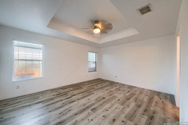 an empty room with wooden floor ceiling fan and windows