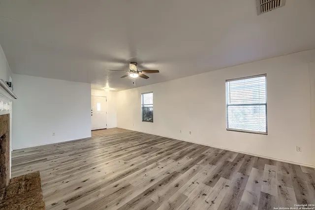an empty room with wooden floor chandelier fan and windows