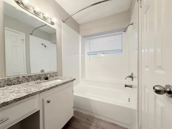 a bathroom with a granite countertop sink a mirror a bathtub and shower