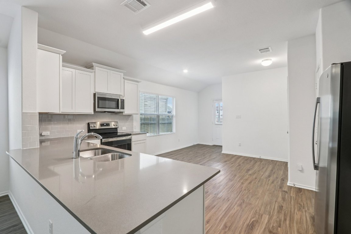 240 Line Of Fire Way Jarrell, TX 76537 - Photo 8 of 33 Kitchen with white cabinetry, appliances with stainless steel finishes, backsplash, a peninsula, and LVP flooring