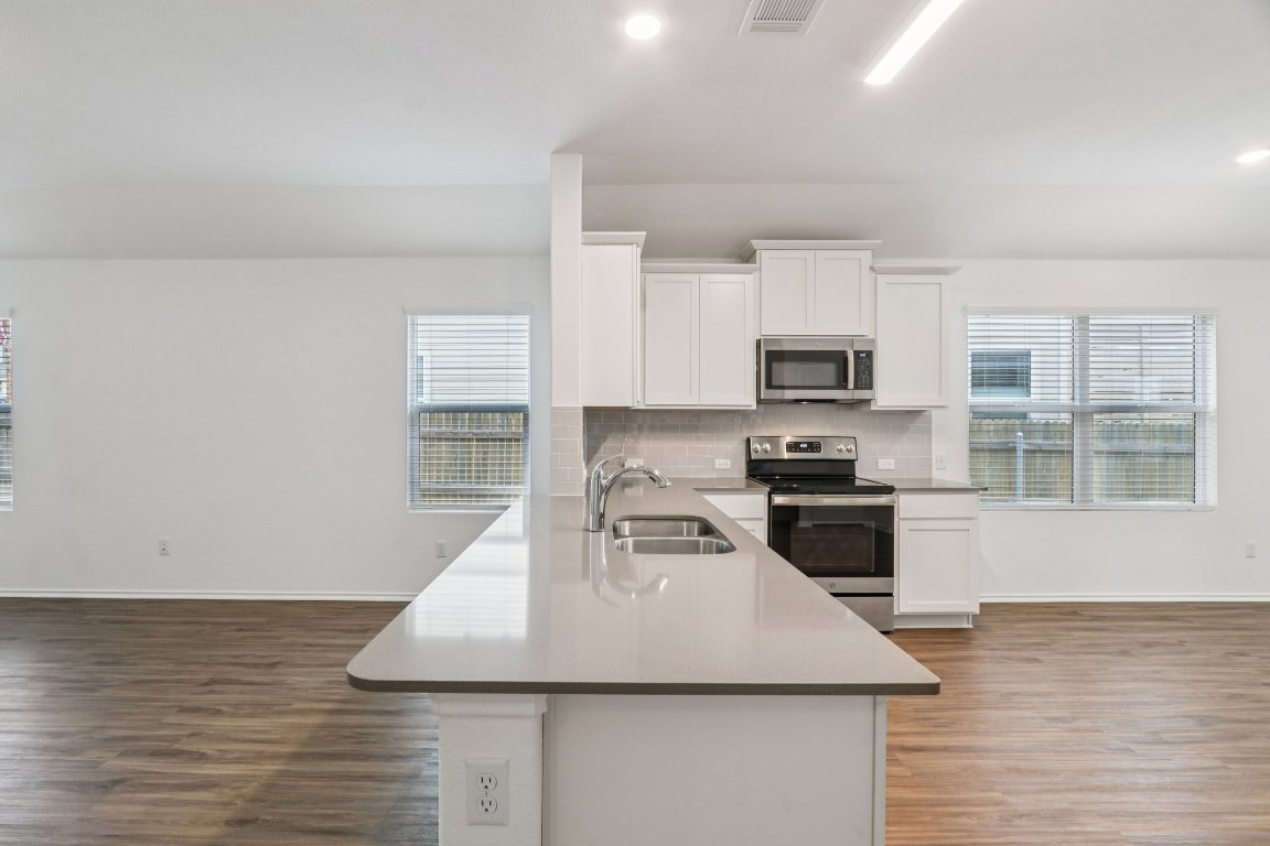 240 Line Of Fire Way Jarrell, TX 76537 - Photo 9 of 33 Kitchen with appliances with stainless steel finishes, white cabinetry, LVP flooring, decorative backsplash, and recessed lighting