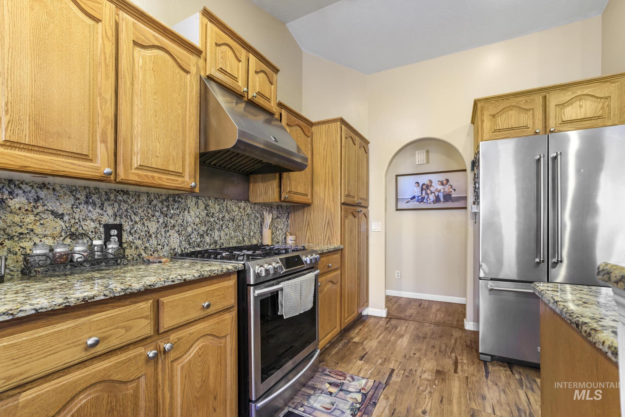 733 Beta Circle Twin Falls, ID 83301 - Photo 8 of 50 Kitchen featuring stainless steel appliances, light stone counters, wood finish cabinets, dark wood finished floors, and tasteful backsplash