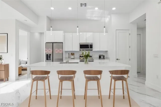 a kitchen with kitchen island granite countertop a dining table chairs refrigerator and cabinets