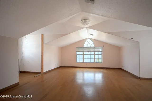 an empty room with wooden floor chandelier and windows