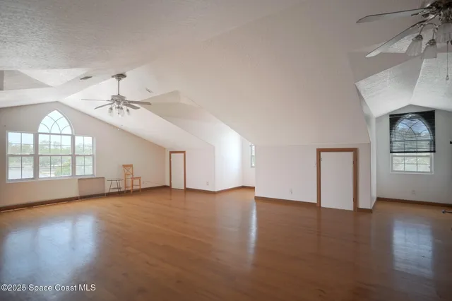 an empty room with wooden floor chandelier fan and windows