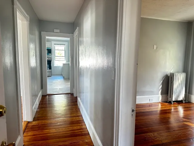 a view of a hallway with wooden floor and a bathroom